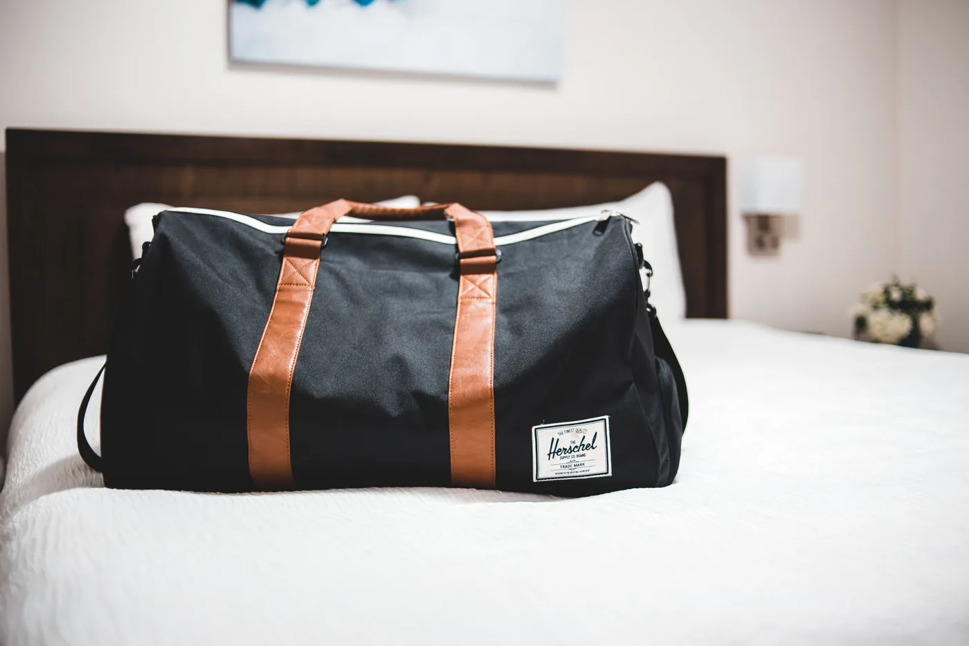 A weekender duffel bag sitting on a made hotel bed