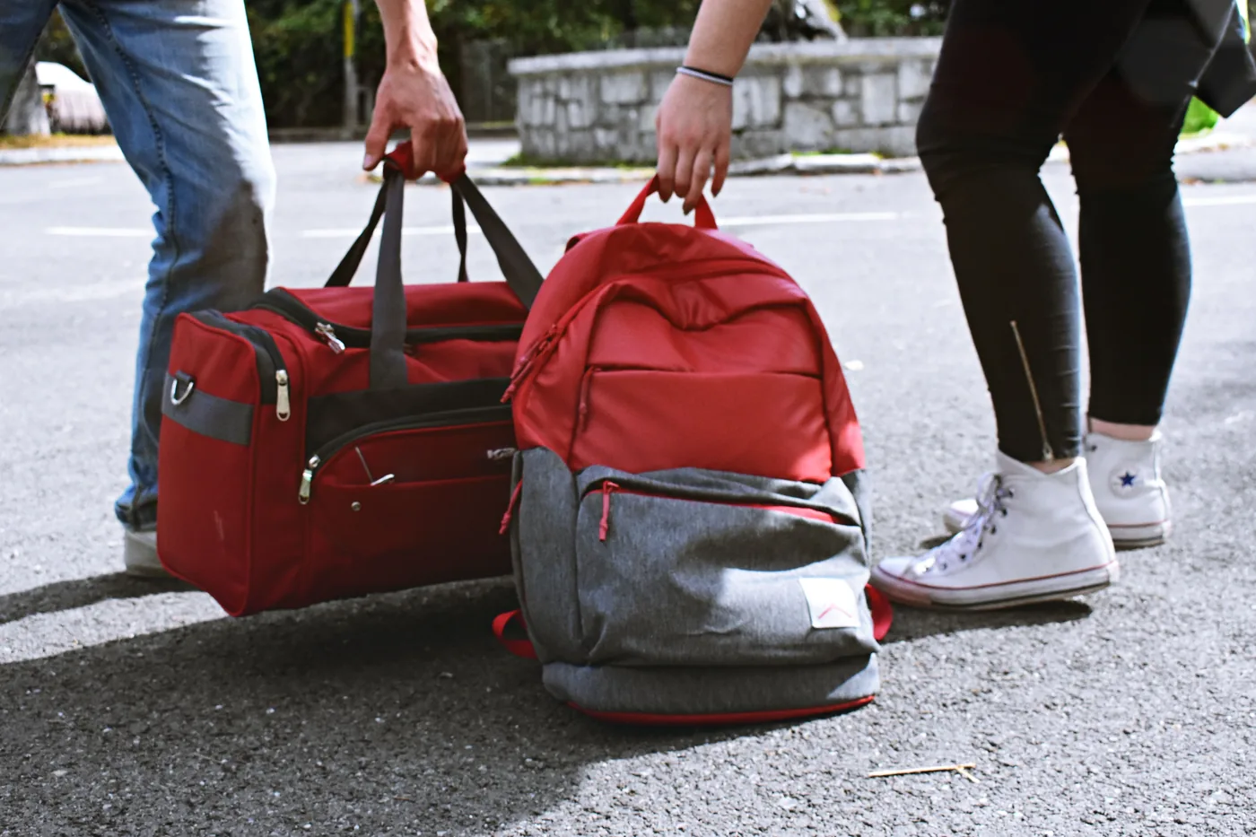 Two travelers setting down a duffel bag and a backpack on the pavement